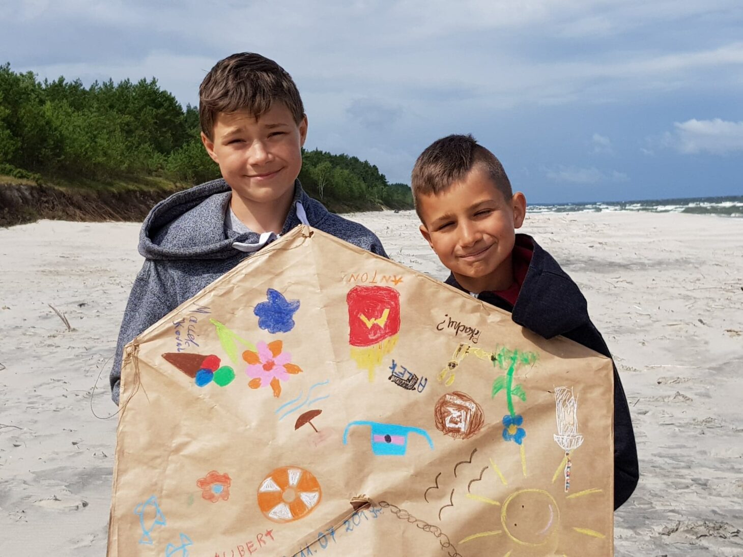 Dwaj chłopcy pokazują papierowy parasol na plaży.