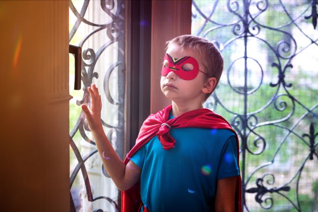 Chłopiec w czerwonej masce i pelerynie opiera się ręką o okno - sesja fotograficzna kampanii OKNO