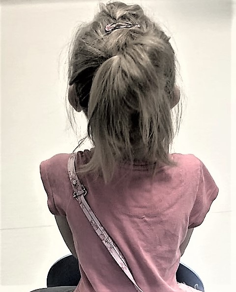 Kilkuletnia dziewczynka w różowej bluzeczce siedząca tyłem, blondynka, włosy związane w kitkę