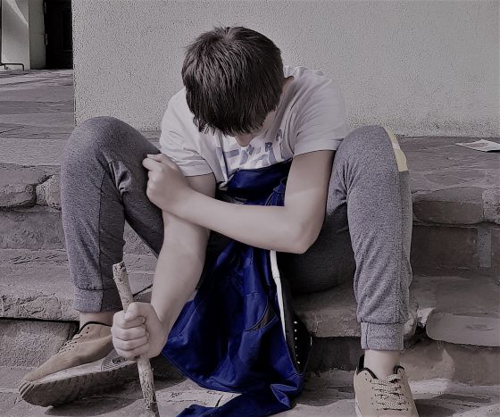 Chłopiec, nastolatek siedzący na schodach piszący patykiem po ziemi