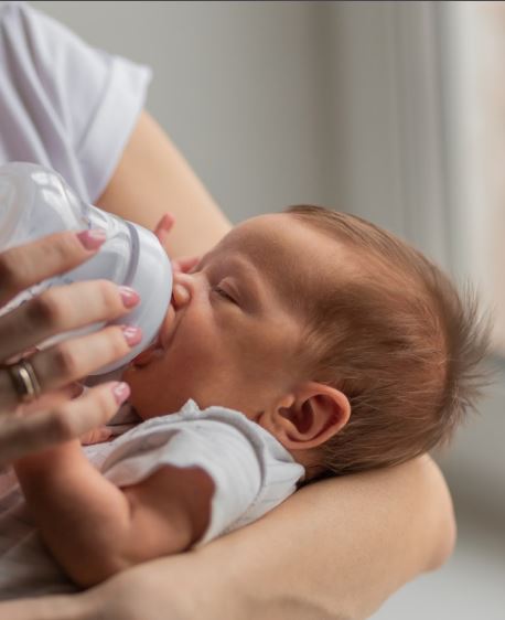 niemowlę karmione butelką dłoń opiekunki trzyma butelkę