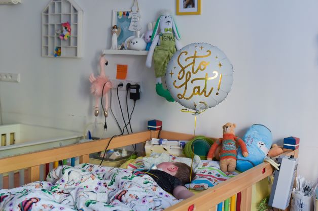 dziecko w łóżeczku medycznym hospicjum balon z napisem sto lat