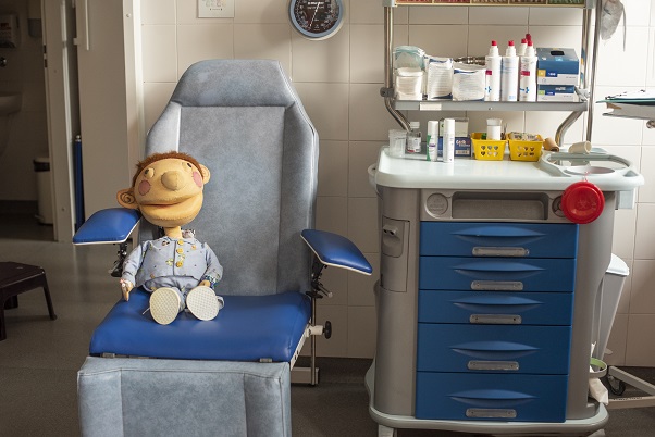 onkologia lalka Edek siedzaca w fotelu w pizamce w pokoju zabiegowym pobyt w szpitalu i leczenie dochodzace poradnik onkologiczny