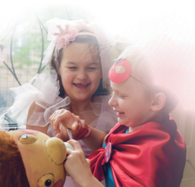 Chłopczyk w stroju superbohatera i dziewczynka w stroju księżniczki bawią się z lalką terapeutyczną