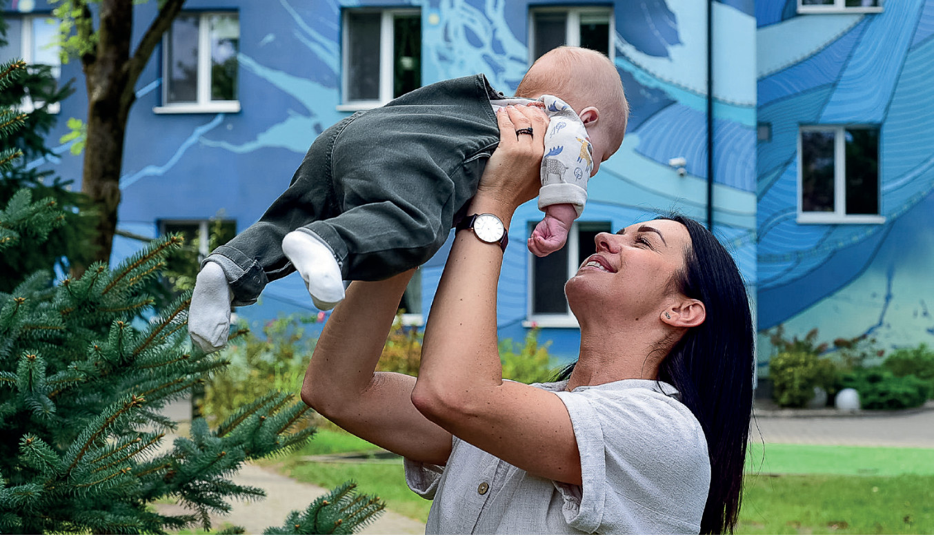 Zdjęcie w „Kwartalnik Gajusz zimą 04/25” przedstawiające dziecko podnoszone przez opiekunkę w Interwencyjnym Ośrodku Preadopcyjnym Tuli Luli.